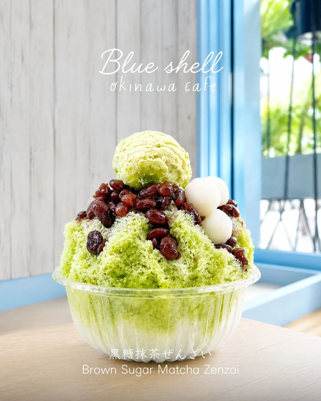 透明な器に盛られた抹茶かき氷に抹茶アイス、小豆、白玉がトッピングされた写真。「Blue shell okinawa cafe」「黒糖抹茶ぜんざい Brown Sugar Matcha Zenzai」の文字入り。