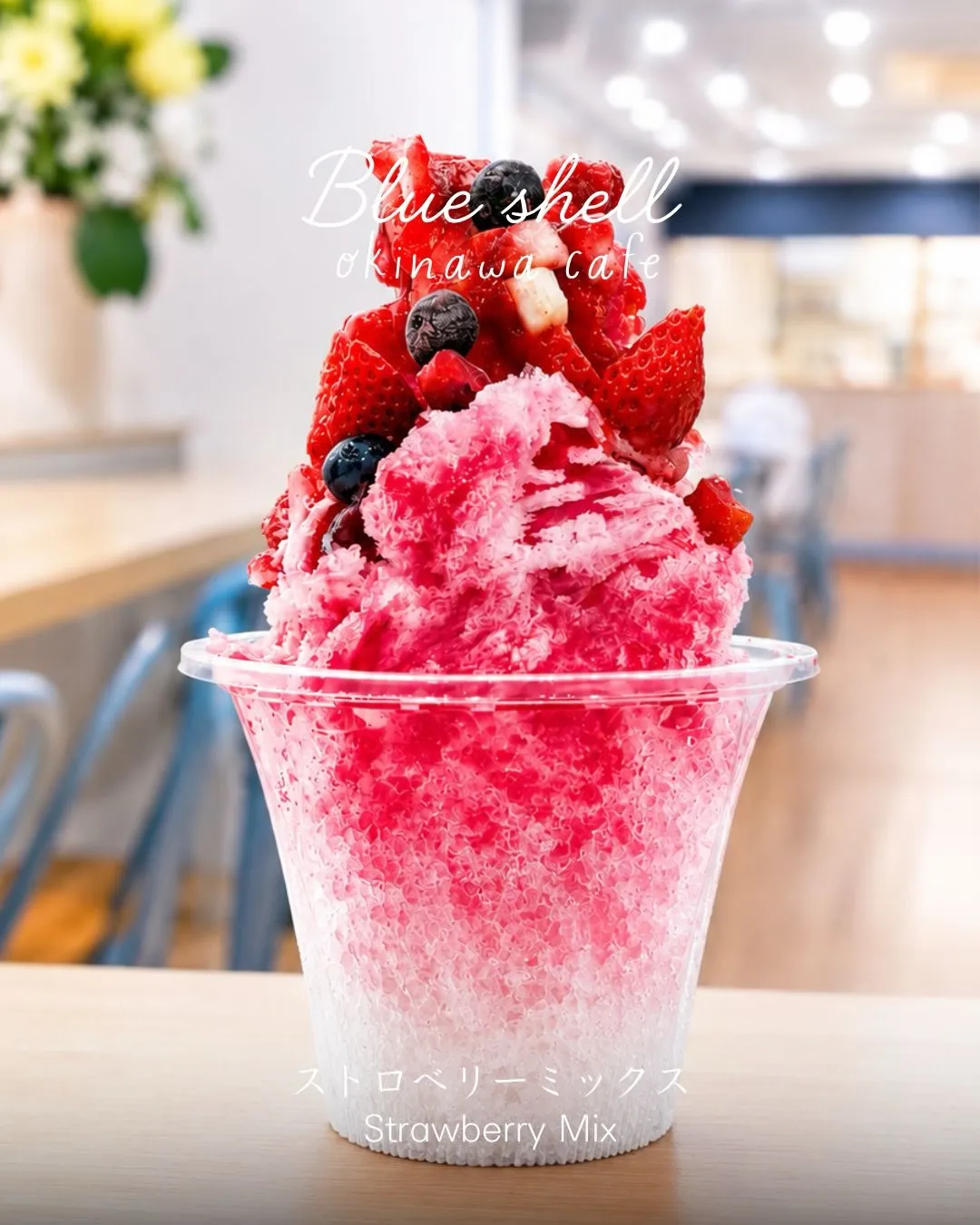 テーブルに置かれた、イチゴやブルーベリーがトッピングされた赤いかき氷。「Blue shell okinawa cafe」「ストロベリーミックス Strawberry Mix」の文字入り。