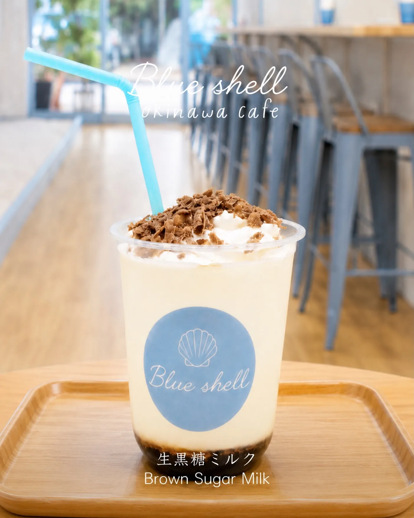 カフェの店内でトレイに載せられたドリンク「生黒糖ミルク Brown Sugar Milk」。カップには「Blue shell」のロゴシールが貼られ、上部には「Blue shell okinawa cafe」の文字が入っている。